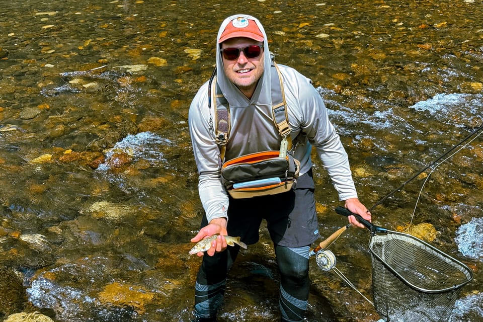 An angler crouching in a shallow stream with a landing net