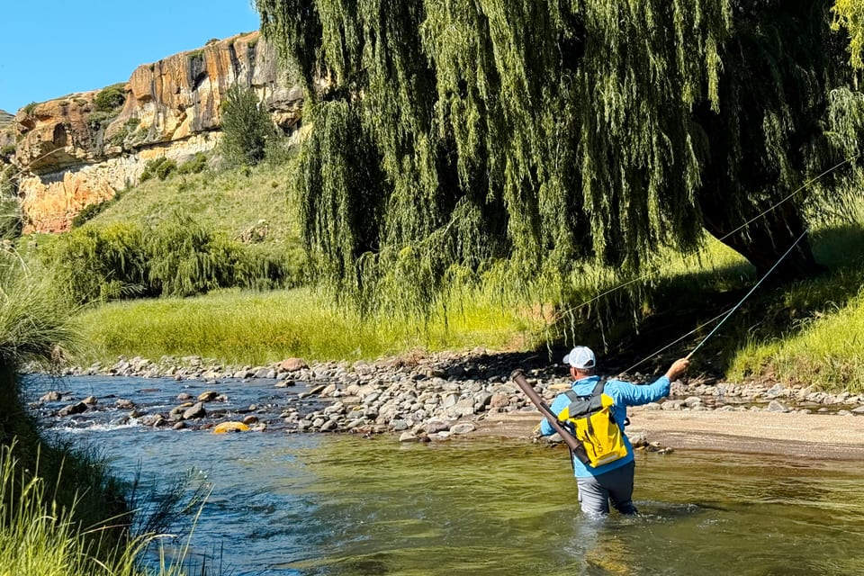 A fly fisherman casting in the river below the sandstone cliffs