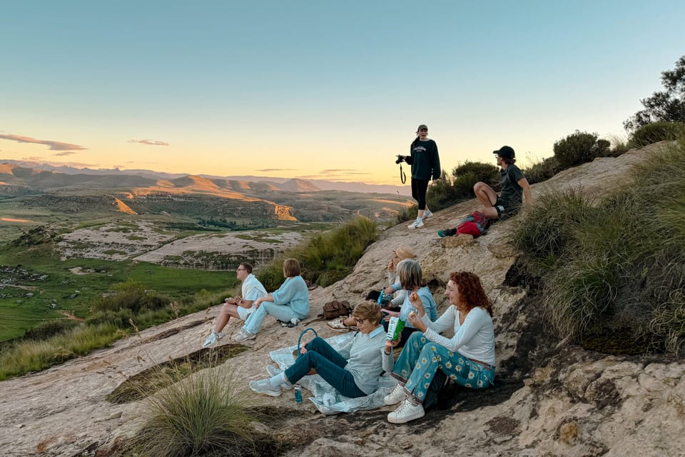 Friends sitting on a rocky outcrop watching the sun set over the valley