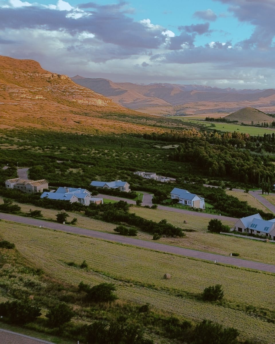 Estate homes among green belts at golden hour, with the valley running out to the Maluti mountains