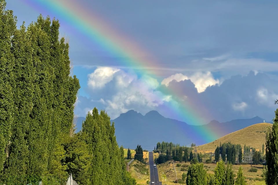 A rainbow arching over the mountains behind a row of poplars